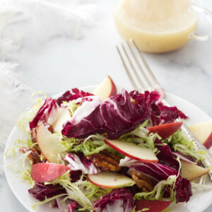 A salad serving of radicchio frisée salad and a small pitcher of lemon-honey vinaigrette in the background.
