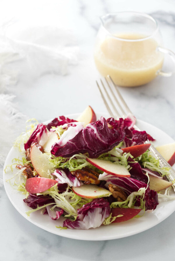 A salad serving of radicchio frisée salad and a small pitcher of lemon-honey vinaigrette in the background.