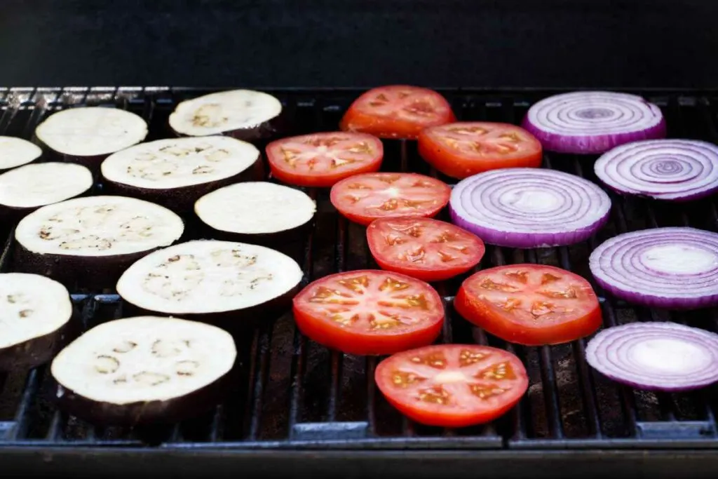 Slices of eggplant, tomato and red onion on a grill.