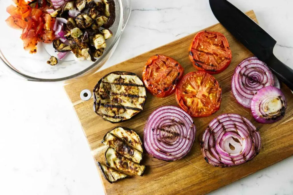 Cutting grilled, eggplant, onion, and tomatoes on a cutting board.