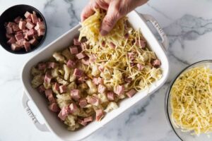 Adding a layer of shredded cheese. Cubed ham in the upper left corner and shredded cheese in the lower right corner.