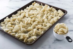A sheet pan with bread chunks ready for drying in the oven. A measuring cup filled with bread chunks in the front lower corner.