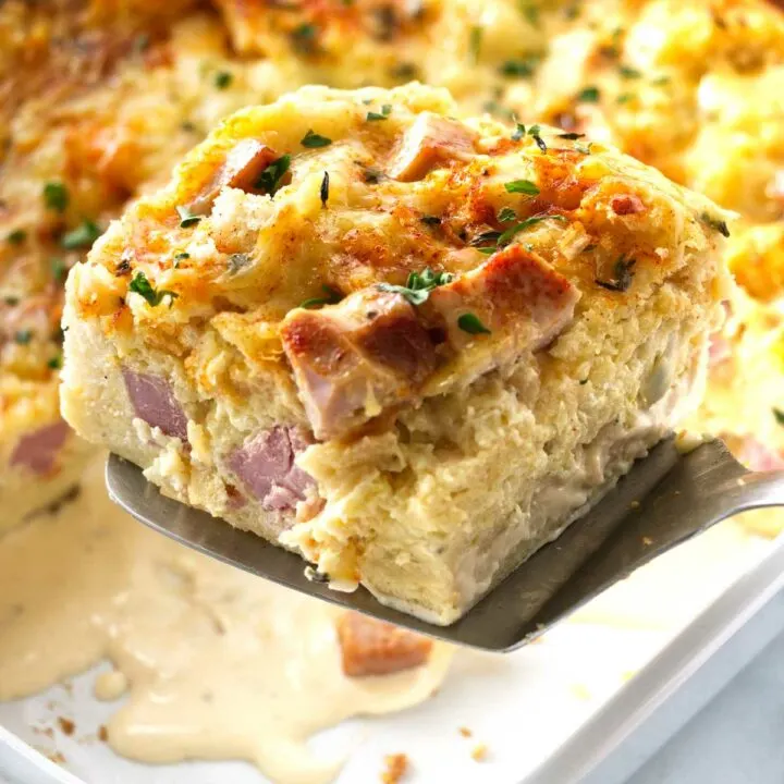 Close up photo of a spatula lifting a serving of ham and cheese strata from the casserole dish.