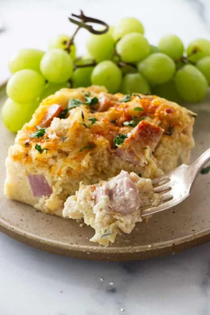 A dinner fork with a bite of the serving of ham and cheese strata.