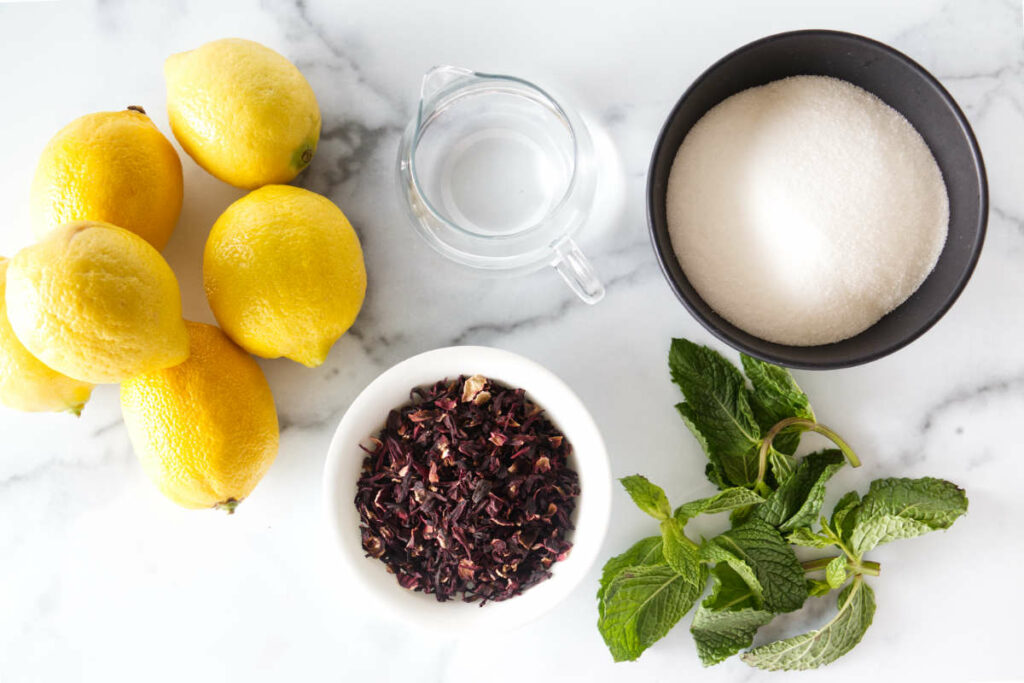 Ingredients for lemonade: sugar, lemons, water, hibiscus flowers, and mint.