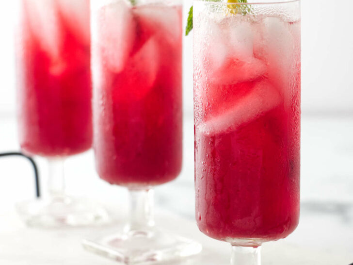 Three glasses of vibrant red lemonade made with hibiscus flowers, garnished with fresh mint leaves.