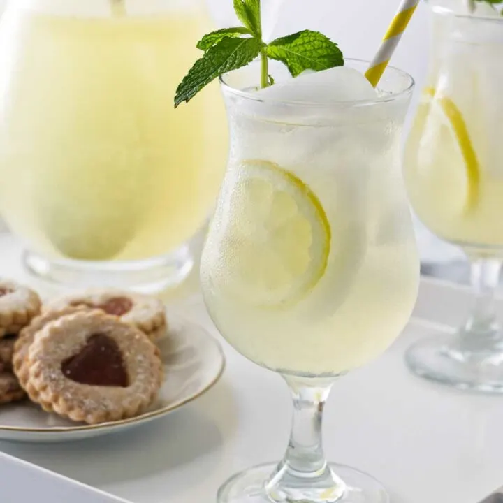 A tray with glasses of old fashioned lemonade garnished with fresh mint, a pitcher of lemonade and a plate of cookies.