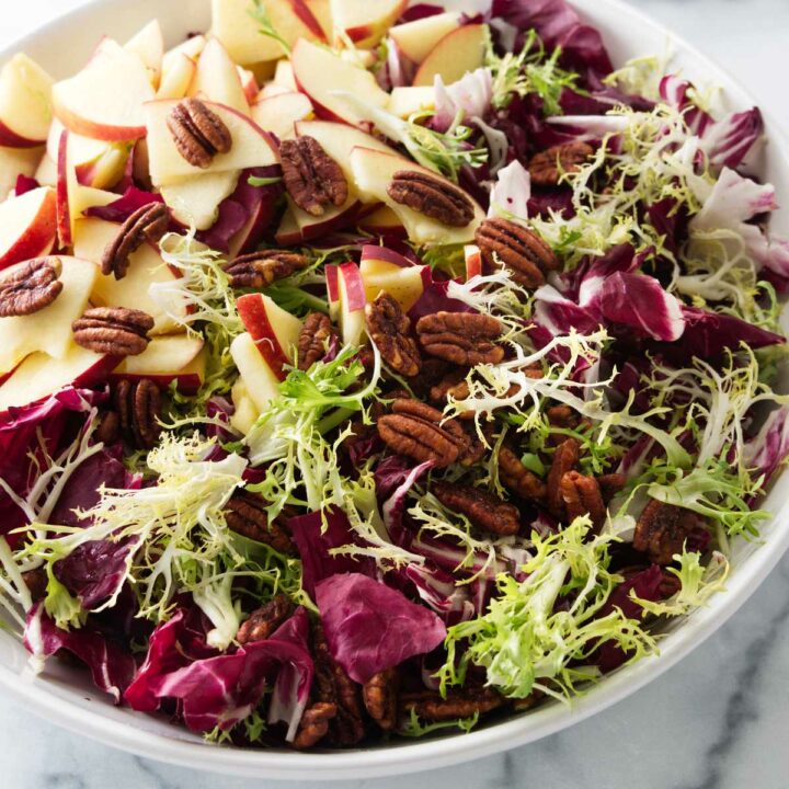 A bowl of radicchio frisée salad with apple slices and candied pecans.