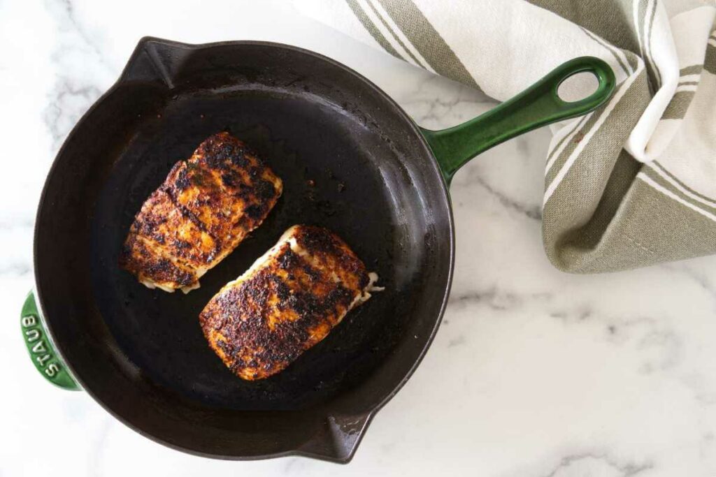 Two filets of halibut with blackening seasoning in a cast iron skillet.