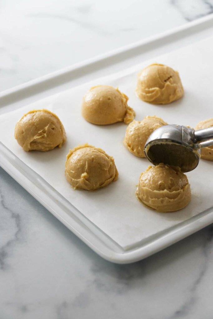 A cookie scoop portioning miso butter onto a parchment-lined white tray.