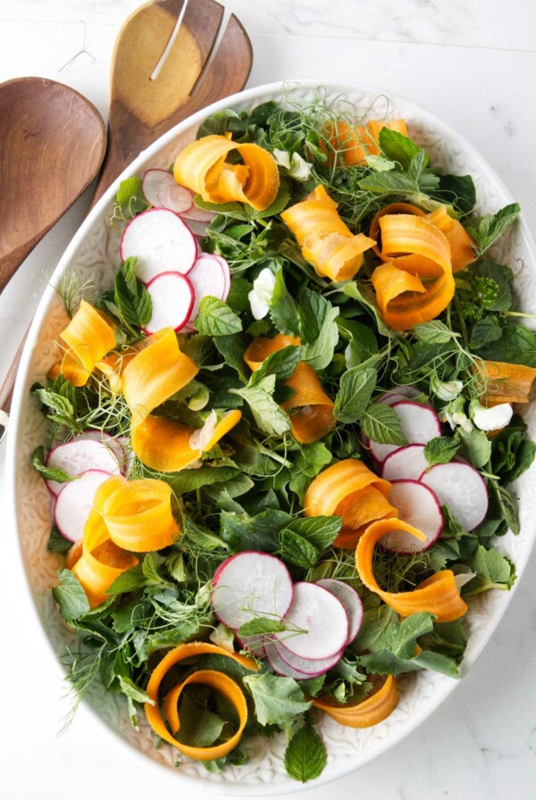 A large serving bowl filled with pea shoots salad next to wooden spoons.