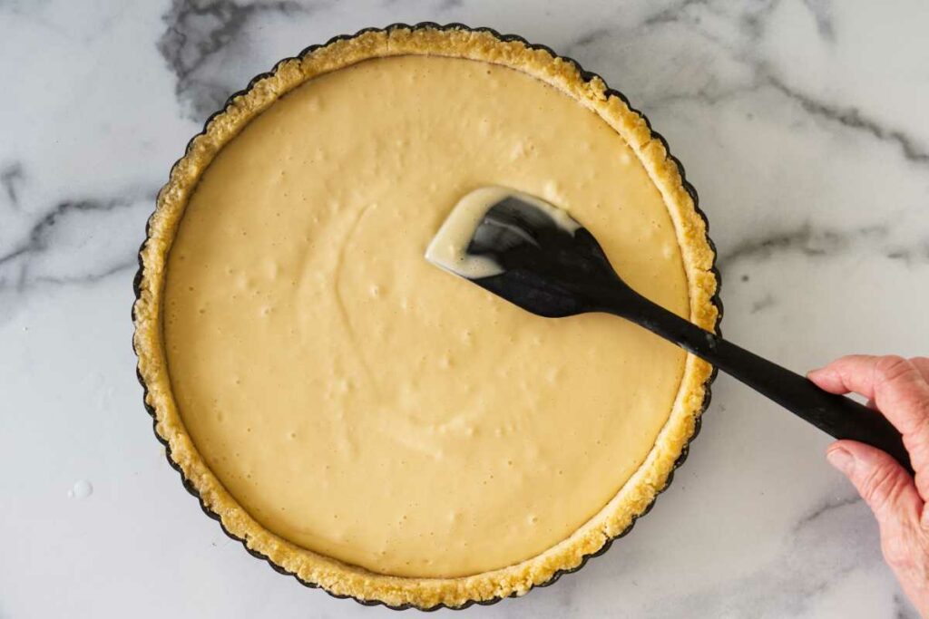 A spatula smoothing the cream cheese batter into the baked tart shell.