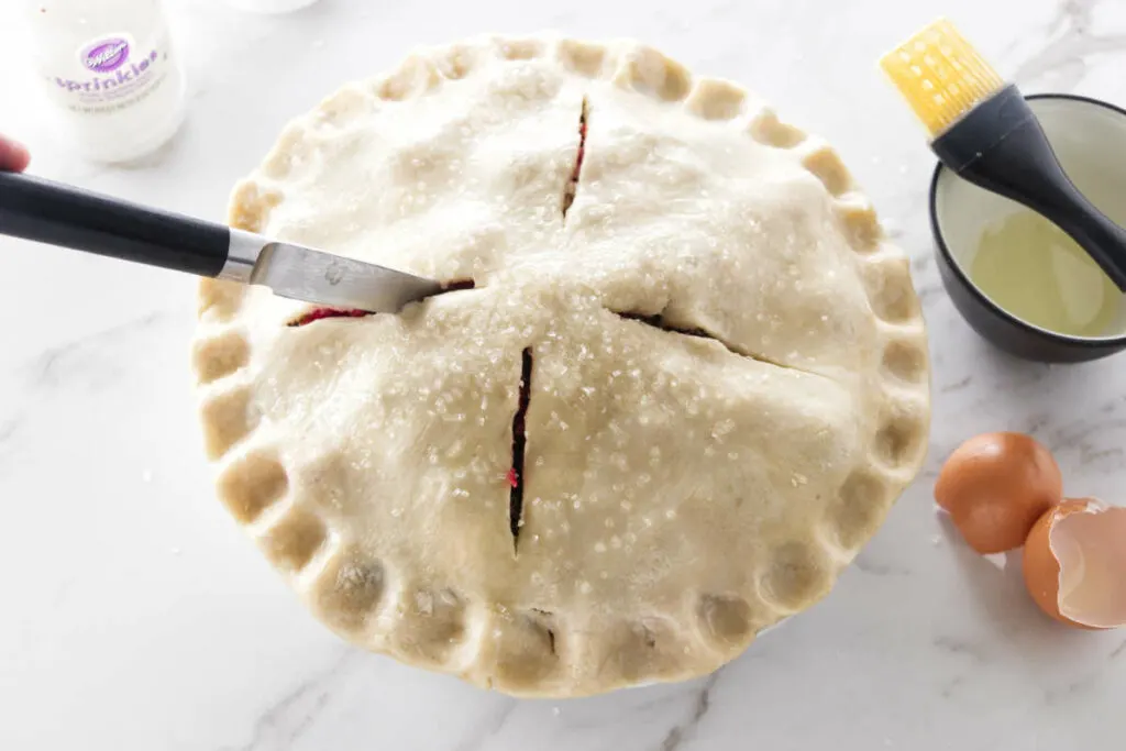 A pie with a paring knife cutting vents in the pastry.