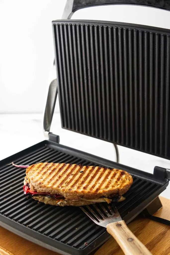 A grilled panini sandwich being lifted off of the panini grill with a spatula.