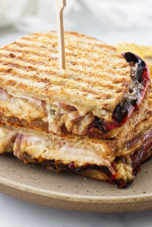 A panini sandwich cut in half and stacked on a plate with a wooden pick inserted in the