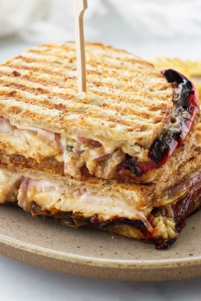 A panini sandwich cut in half and stacked on a plate with a wooden pick inserted in the