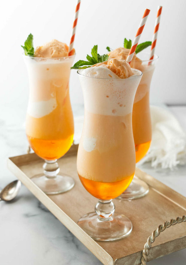 Several glasses of orange creamsicle soda with paper straws.