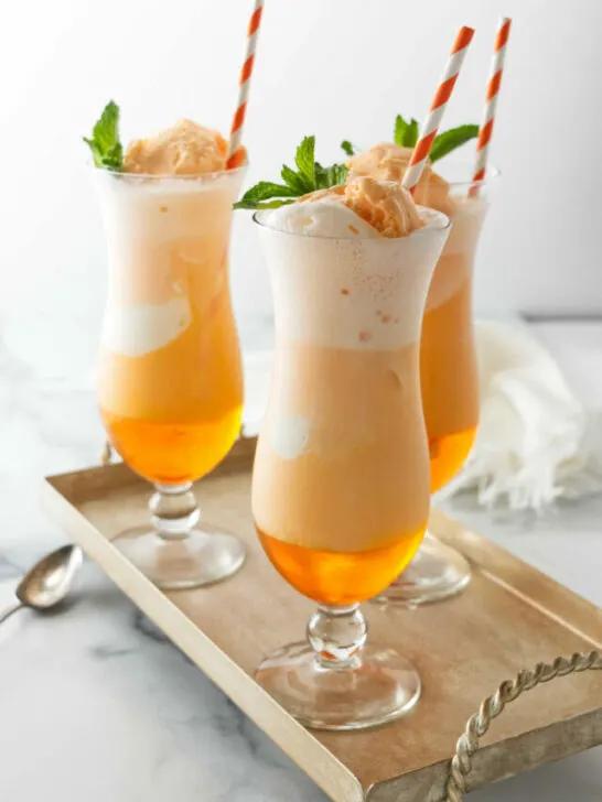 Several glasses of orange creamsicle soda with paper straws.
