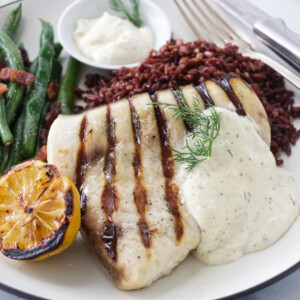 A grilled swordfish on plate with rice, green beans, and a grilled lemon.