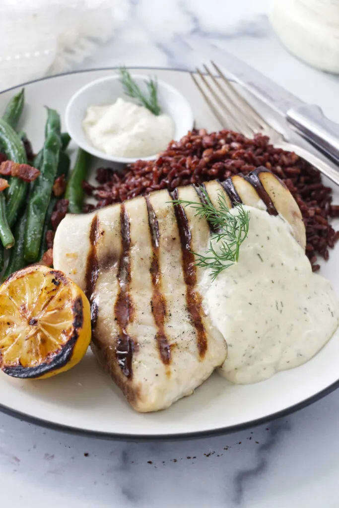 A grilled swordfish on plate with rice, green beans, and a grilled lemon.