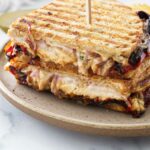 A panini sandwich cut in half and stacked on a plate with a wooden pick inserted in the