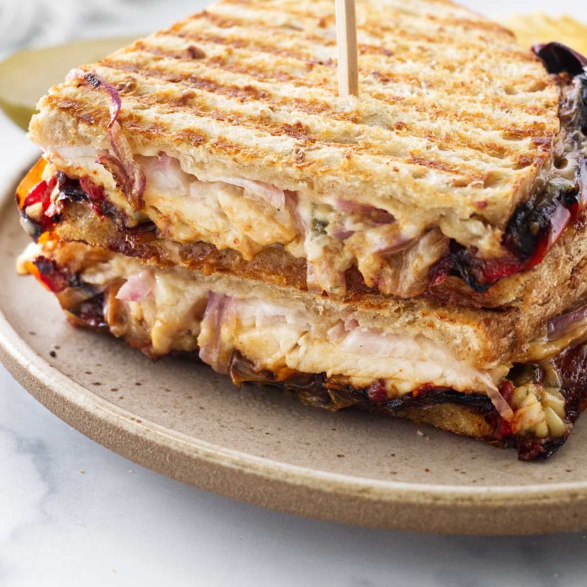 A panini sandwich cut in half and stacked on a plate with a wooden pick inserted in the