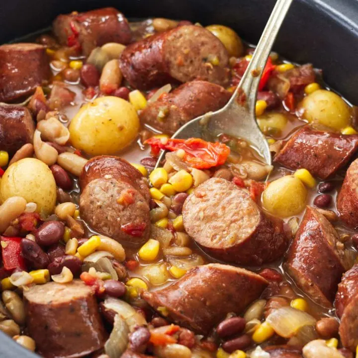 A crockpot with vegetables, sausage and a serving spoon.