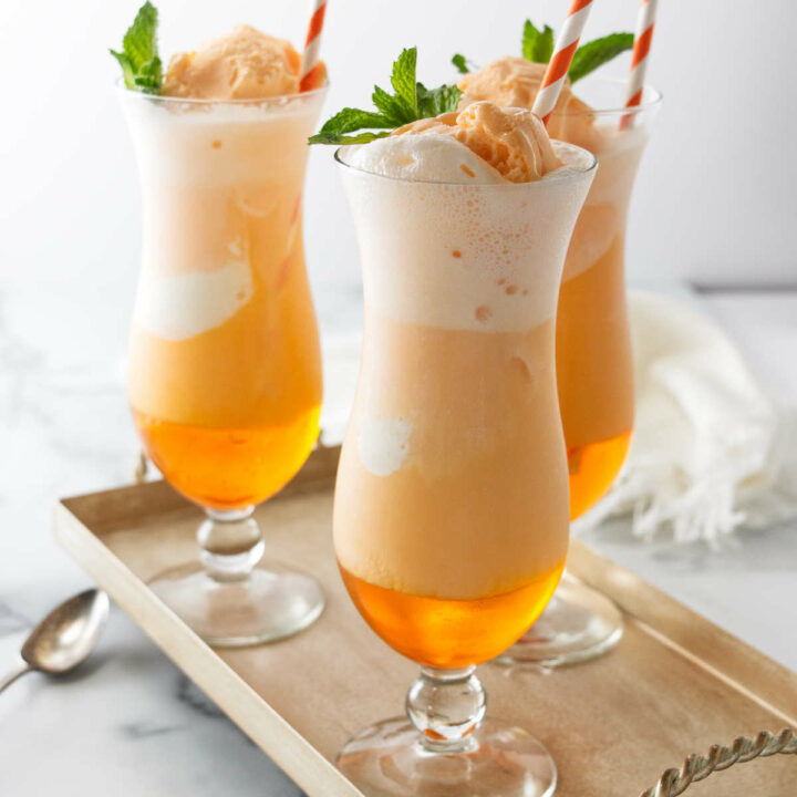 Three orange creamsicle sodas in tall glasses sitting on a serving tray.