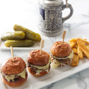 Kraut burger sliders on a plate with French fries. A German mug and pickles are in the background.
