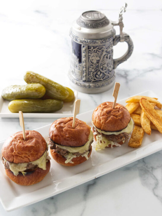 Kraut burger sliders on a plate with French fries. A German mug and pickles are in the background.