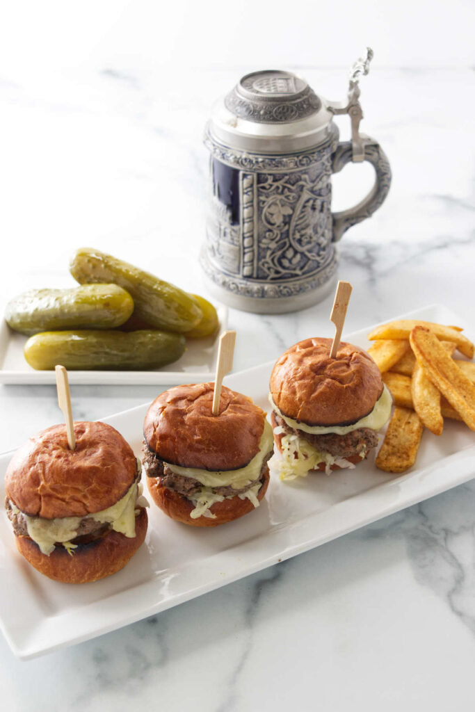 Kraut burger sliders on a plate with French fries. A German mug and pickles are in the background.