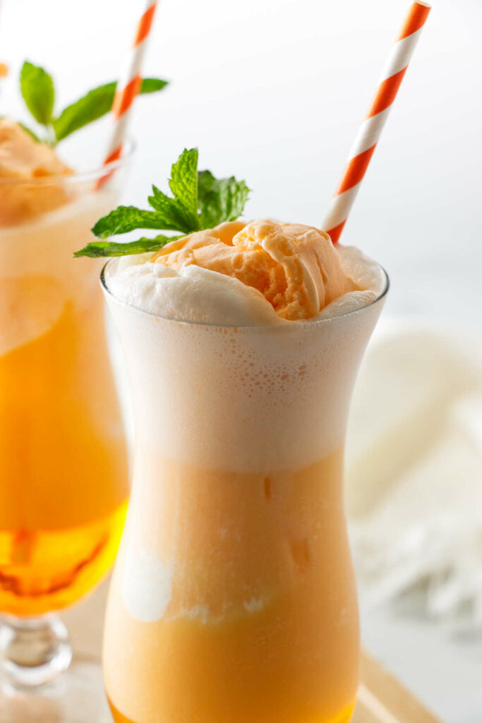 A tall glass with an Italian orange soda with orange sherbet.