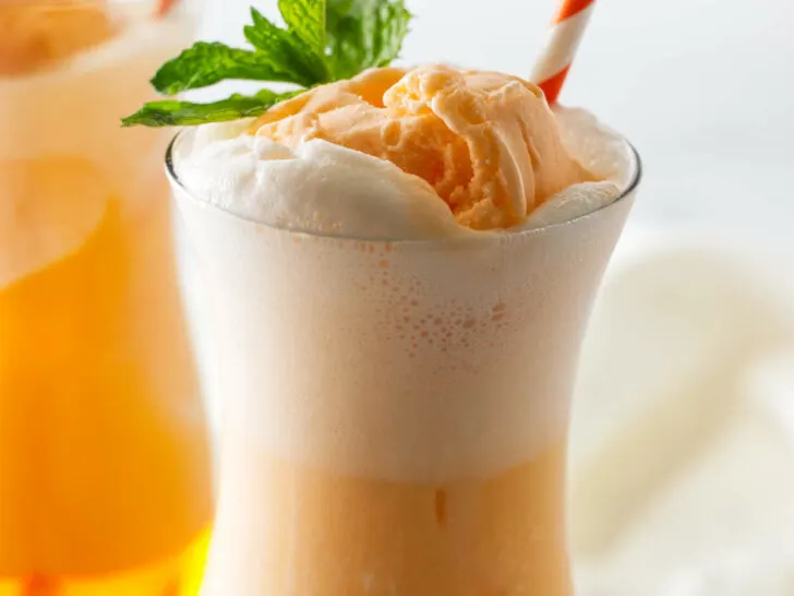 A tall glass with an Italian orange soda with orange sherbet.