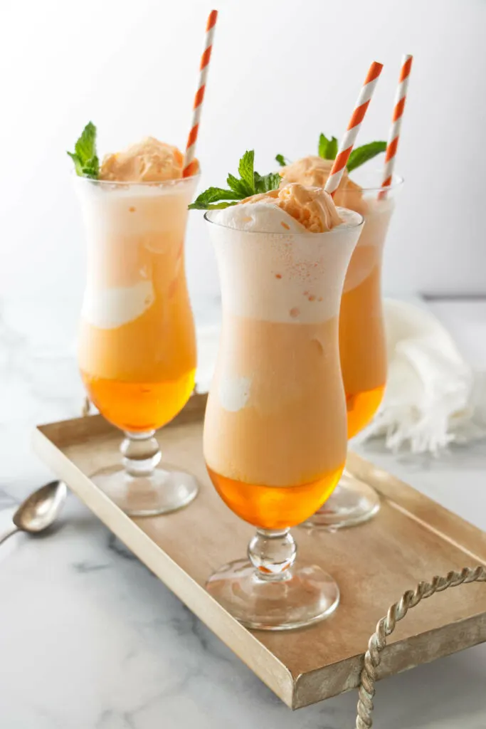 Several glasses of orange creamsicle soda with paper straws.