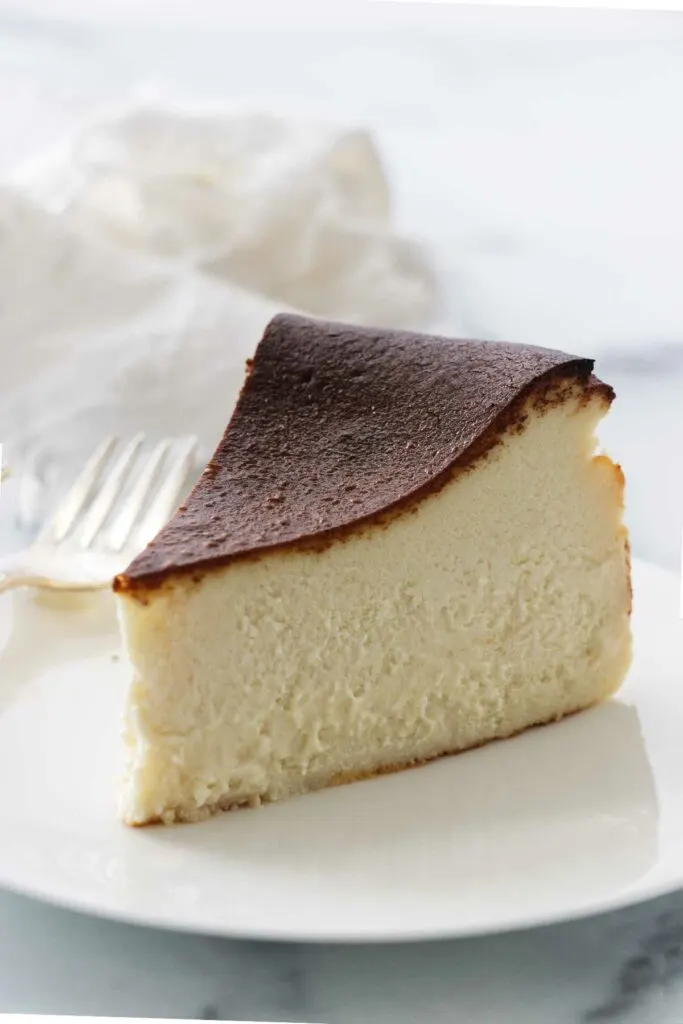 A serving of San Sebastian cheesecake on a white plate with a fork, a napkin in the background.