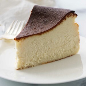 A serving of burnt Basque cheesecake on a white plate with a fork, a napkin in the background.