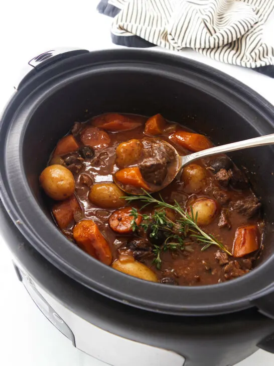 A slow cooker of cooked elk stew and a large serving spoon.