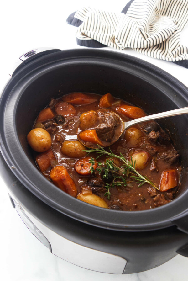 A slow cooker of cooked elk stew and a large serving spoon.