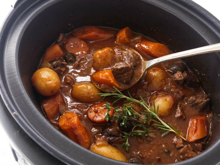A slow cooker of cooked elk stew and a large serving spoon.