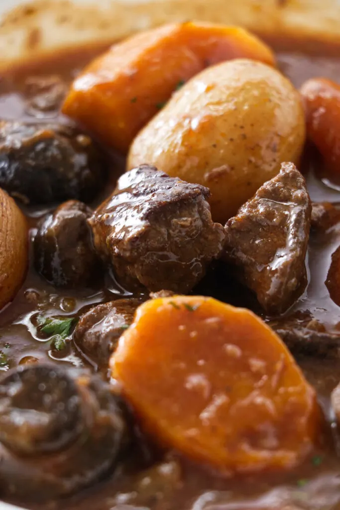 Carrots, mushrooms, elk meat, and potatoes in a serving dish with the cooking sauce.