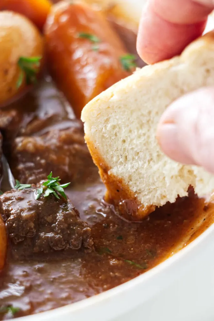 A serving of stew and a chunk of bread being dipped into the sauce.