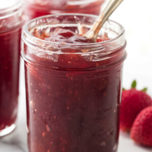 Homemade fresh strawberry jam in a mason jar with a spoon.