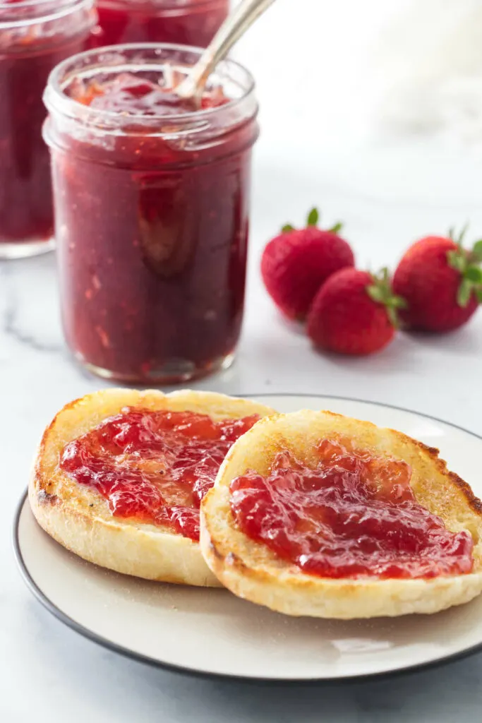 Jars of strawberry jam behind a plate of toast.