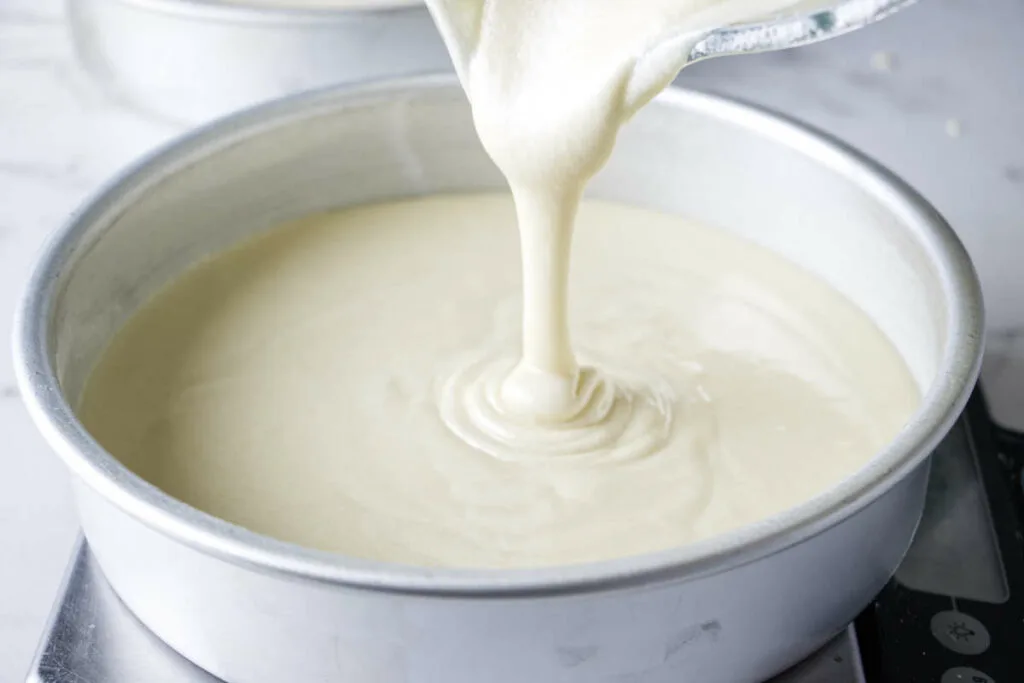 Pouring cake batter into cake pans.