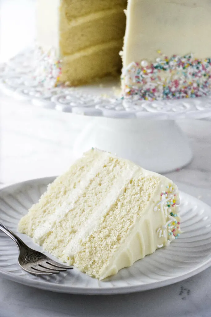 A slice slice of vanilla cake frosted with cream cheese frosting.