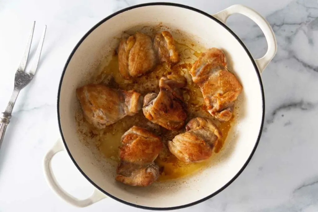 A pot with browned boneless, skinless chicken thighs.