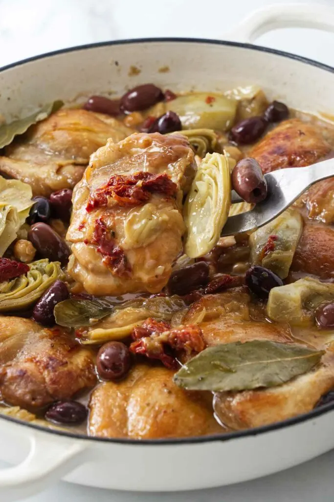 A serving fork with chicken, artichokes, olives and sun-dried tomatoes.