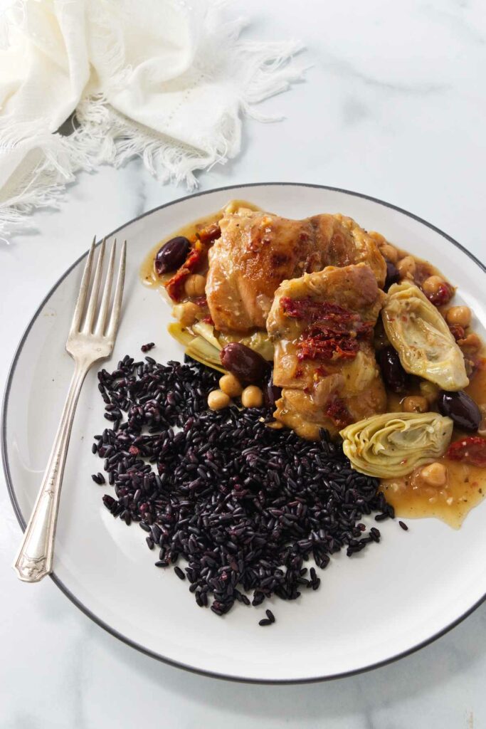 A serving of chicken with artichokes and olives served with black rice.