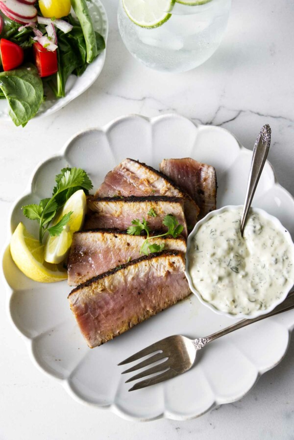 A dinner plate with a sliced tuna steak and some tartar sauce.