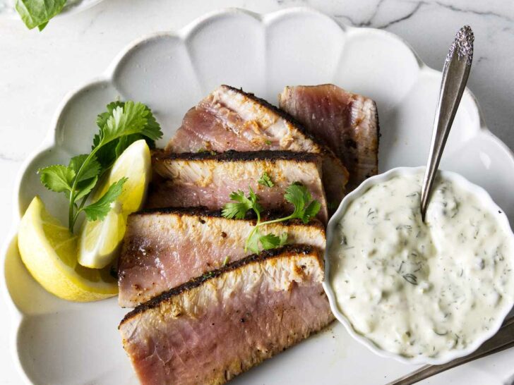 A dinner plate with a sliced tuna steak and some tartar sauce.